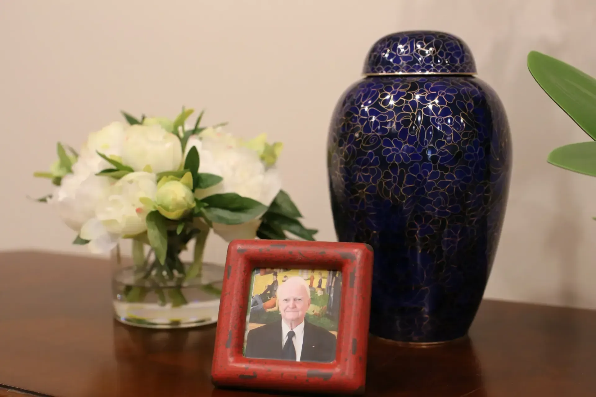 Framed portrait beside a blue vase and white flowers on a wooden table.