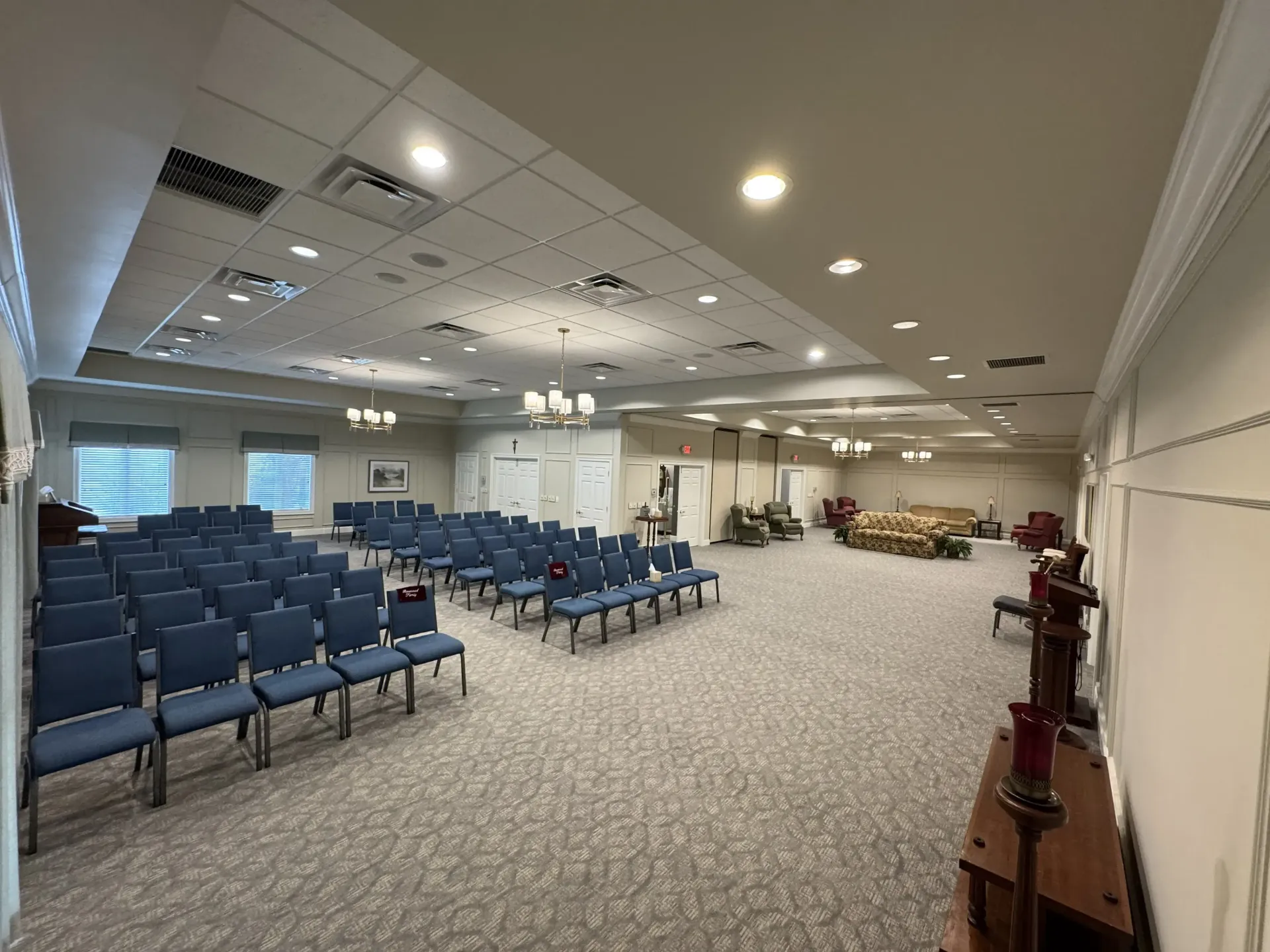 Empty room with rows of blue chairs, carpeted floor, and a small stage area at the front