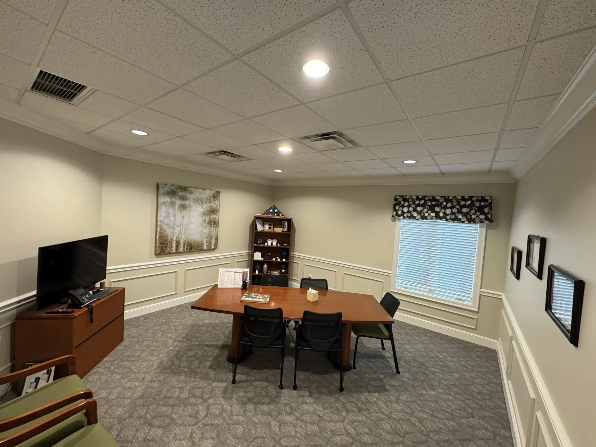 room with table, chairs, TV, and patterned carpet under bright ceiling lights.