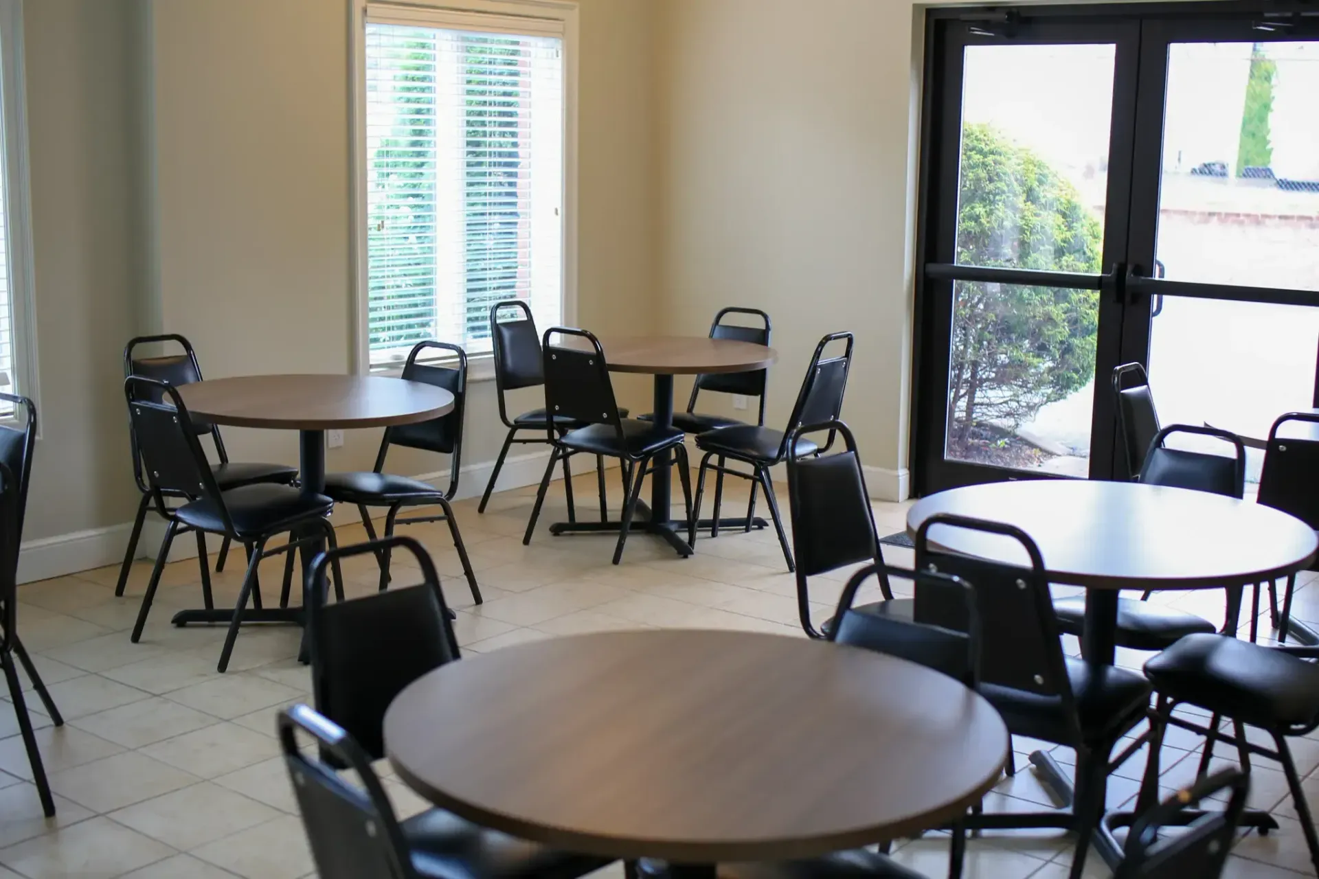Empty room with round tables and black chairs near bright windows