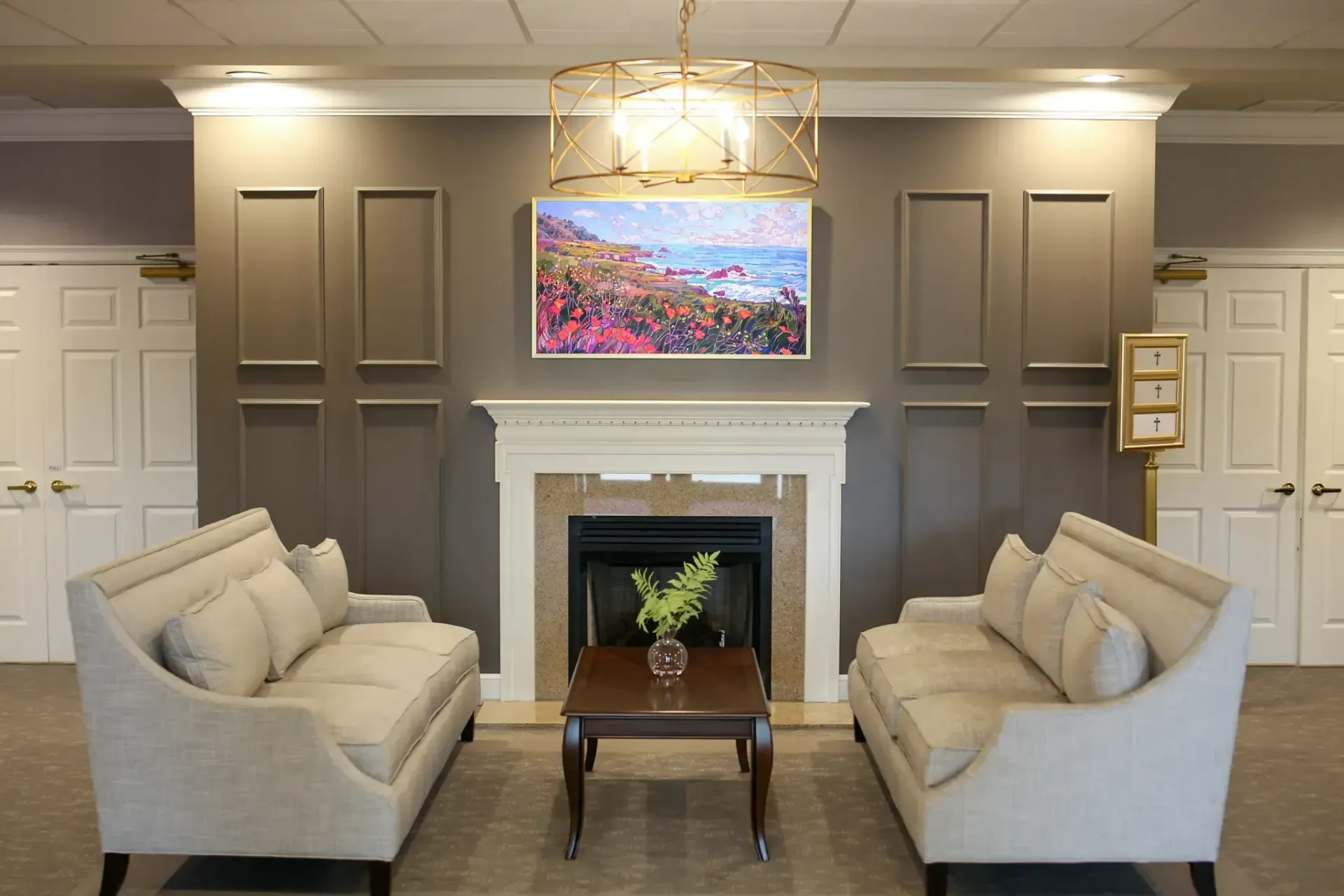 Elegant lounge with two beige sofas, fireplace, and wall-mounted TV in a gray paneled room