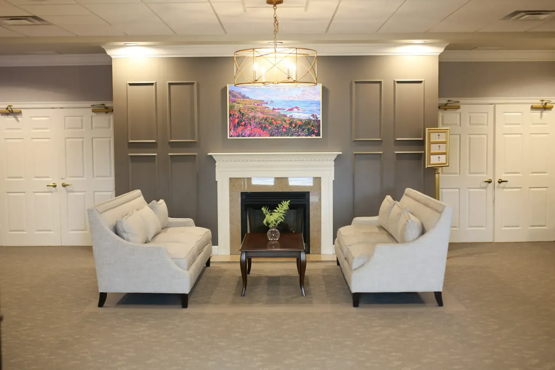 Waiting room with two white sofas facing a fireplace and wall-mounted TV in a beige lobby