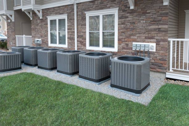 Row of air conditioning units outside a brick building with two windows.