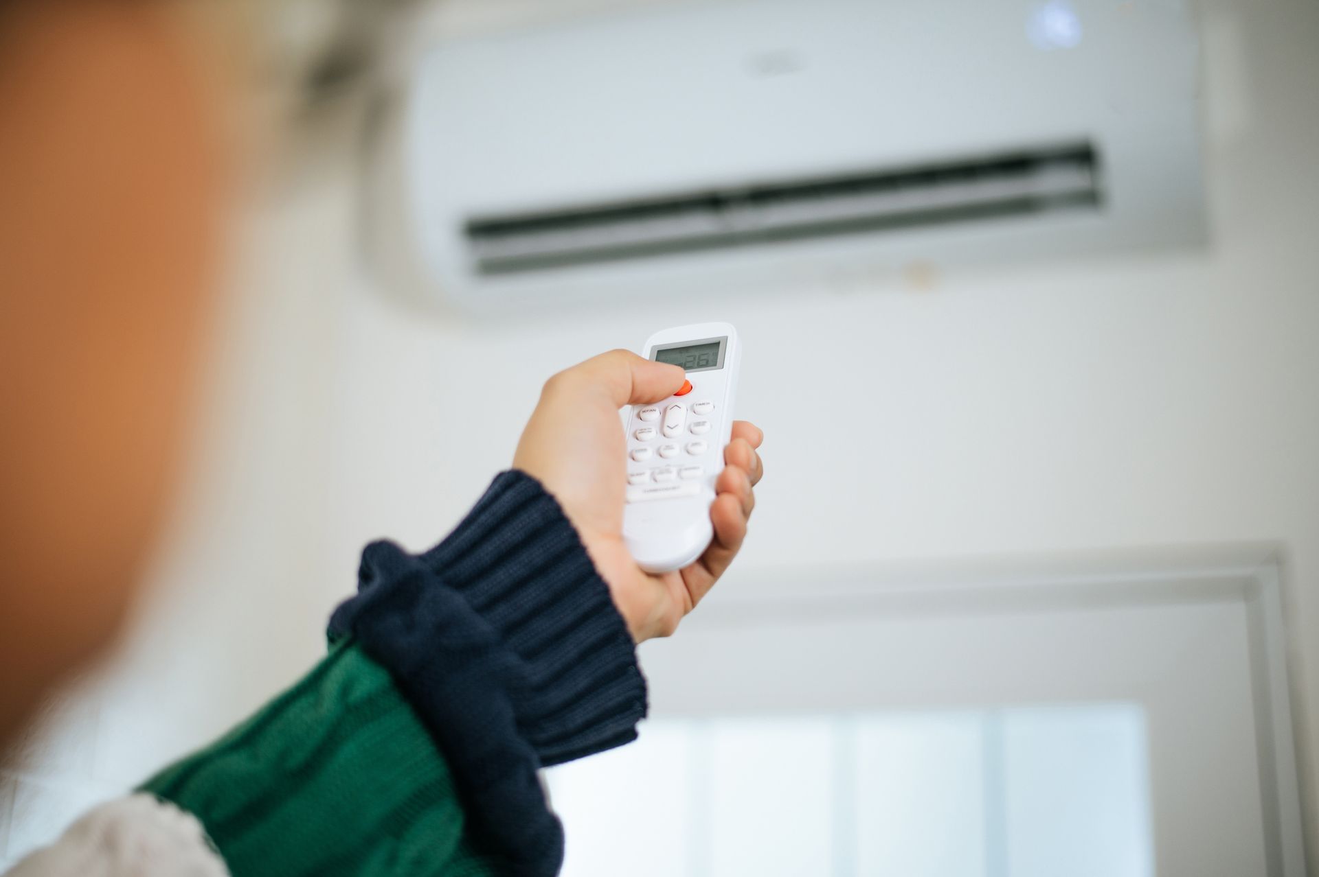 Person holding a remote control, aiming at an air conditioner unit on a wall. Person holding a remote control, aiming at an air conditioner unit on a wall.