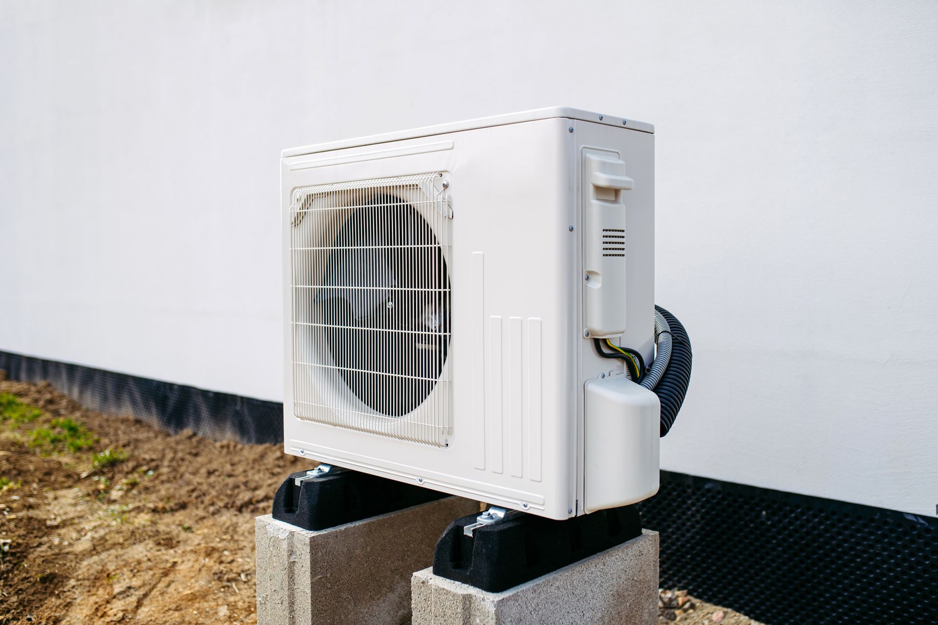 White Air Conditioning Unit Mounted on Concrete Blocks Outdoors — Breezy Point, MN — JM Heating & Air White Air Conditioning Unit Mounted on Concrete Blocks Outdoors — Breezy Point, MN — JM Heating & Air