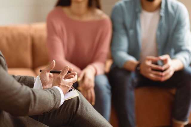 Three people seated in a counseling session, one gesturing while speaking.