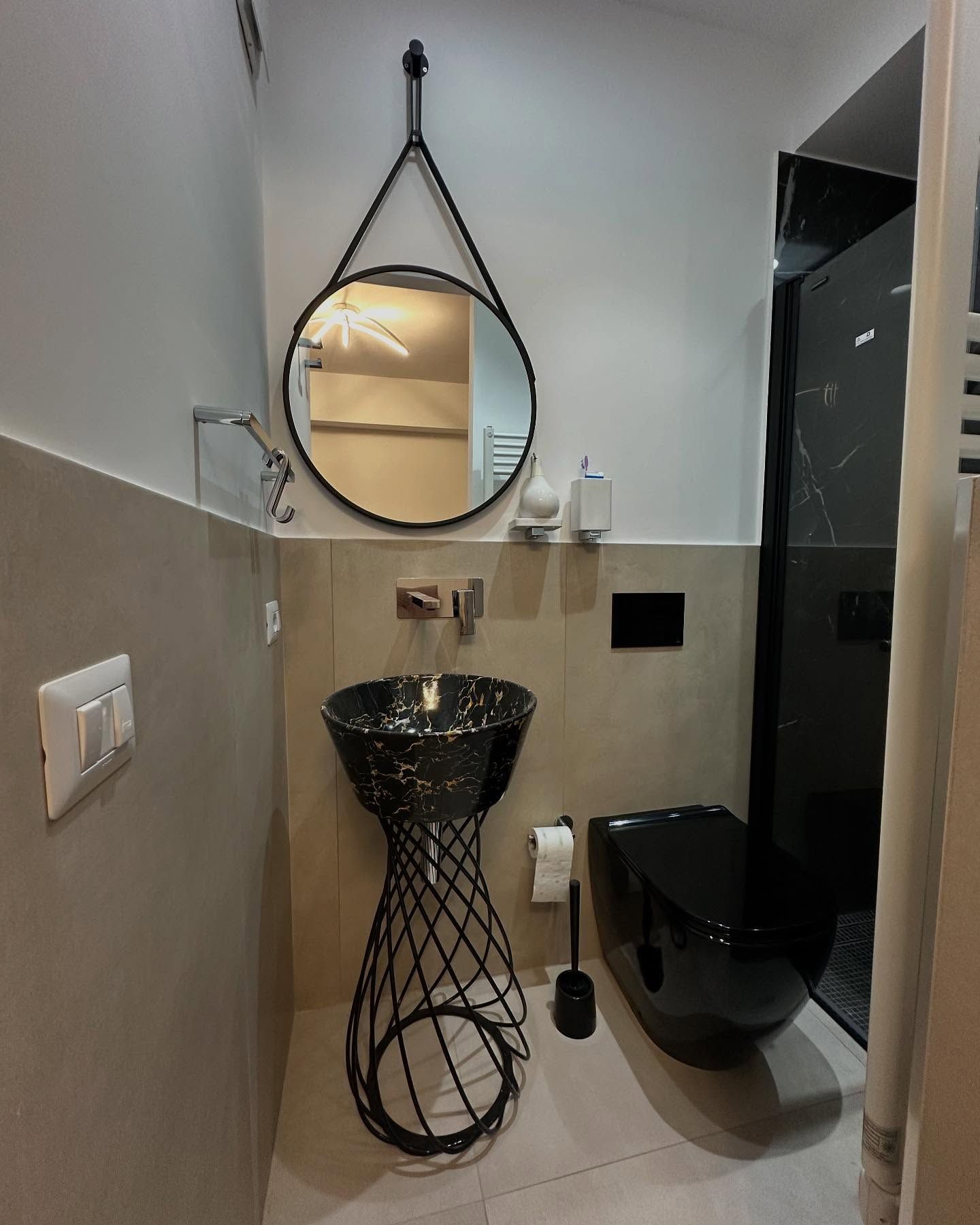 Piccolo bagno con lavabo a colonna nero, specchio ovale e WC accanto a una cabina doccia in vetro.