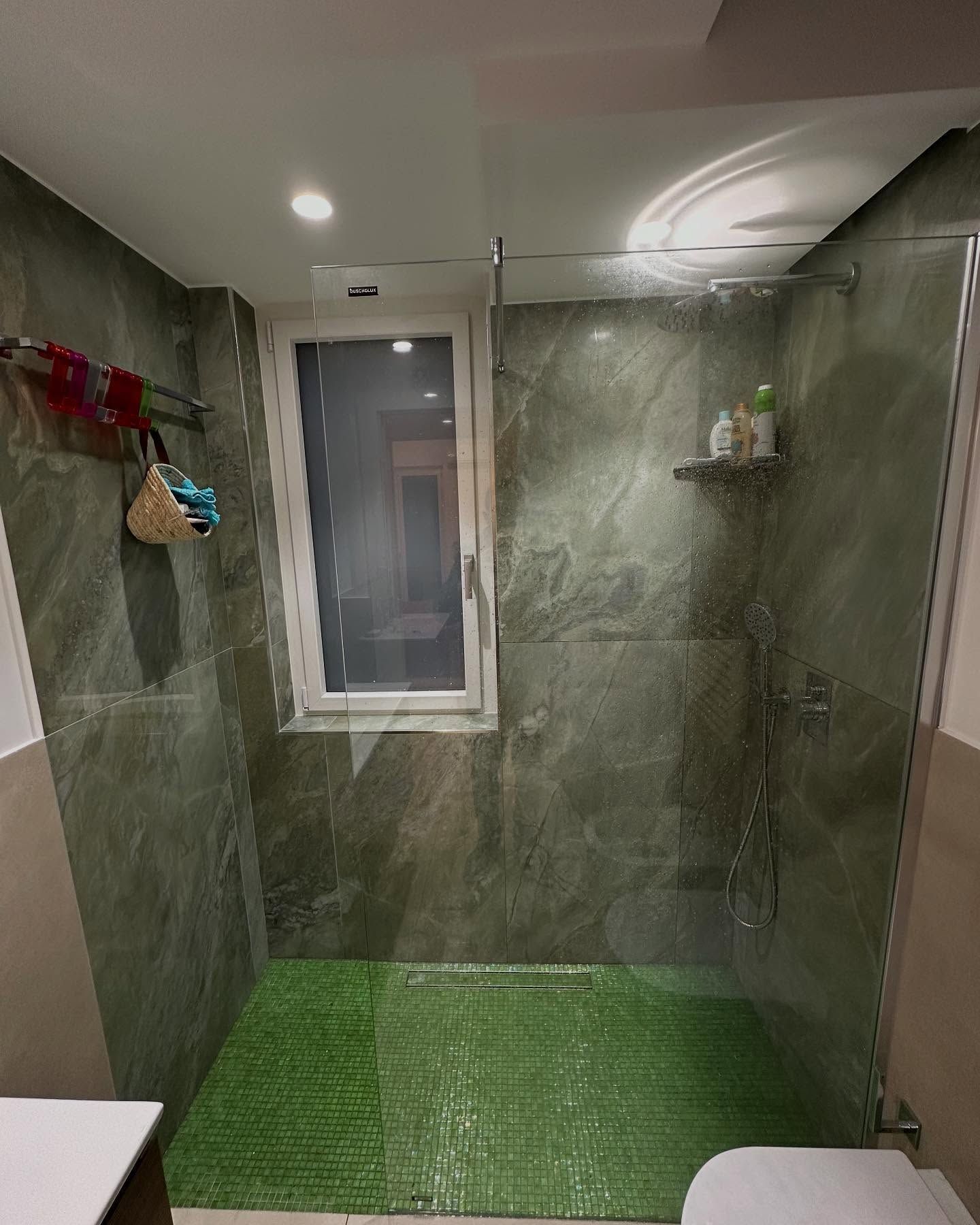 Piccola doccia con piastrelle verdi, porte in vetro e finestra in un bagno moderno.