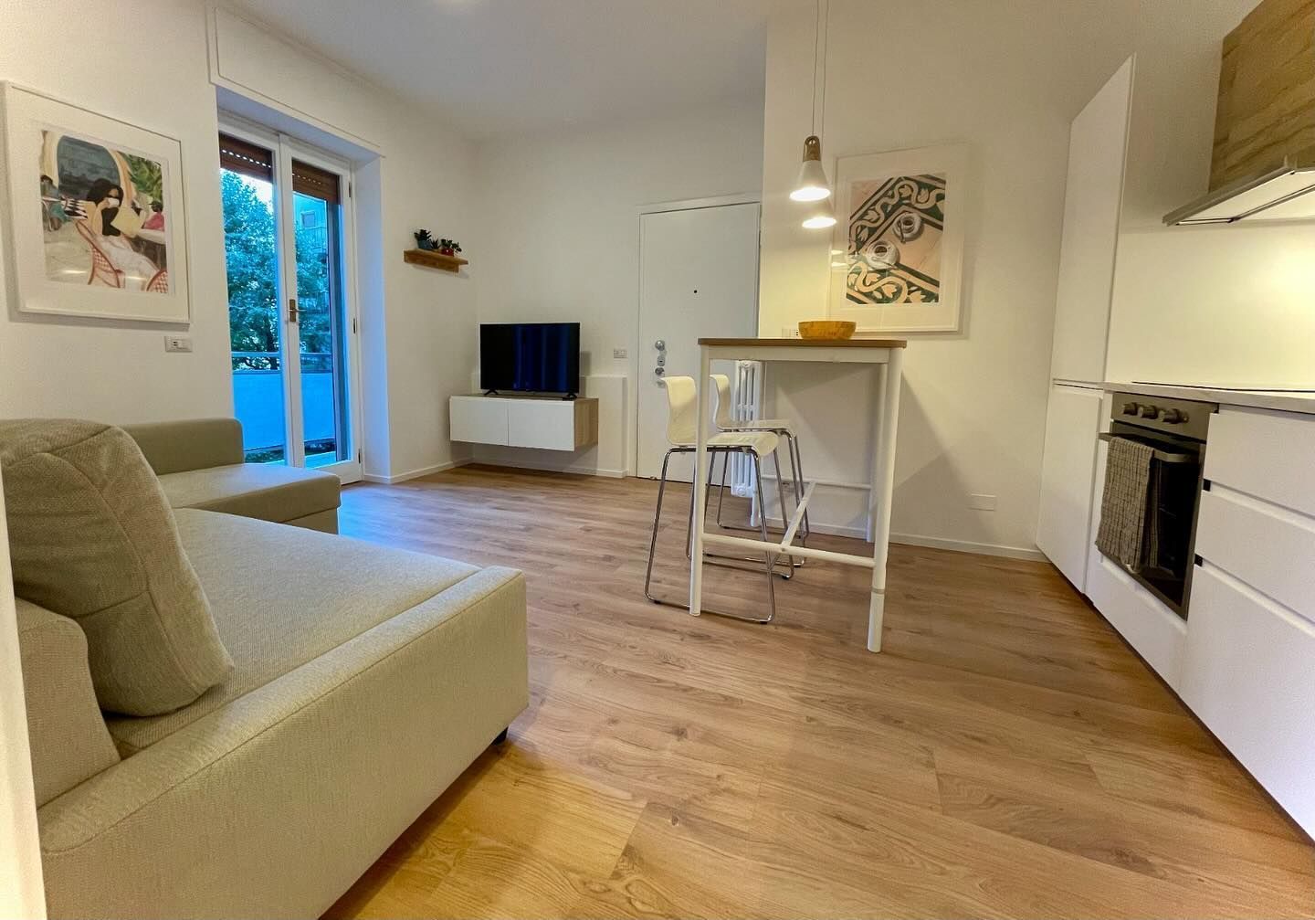 Luminoso monolocale moderno con divano, tavolo da pranzo, TV e cucina a vista.