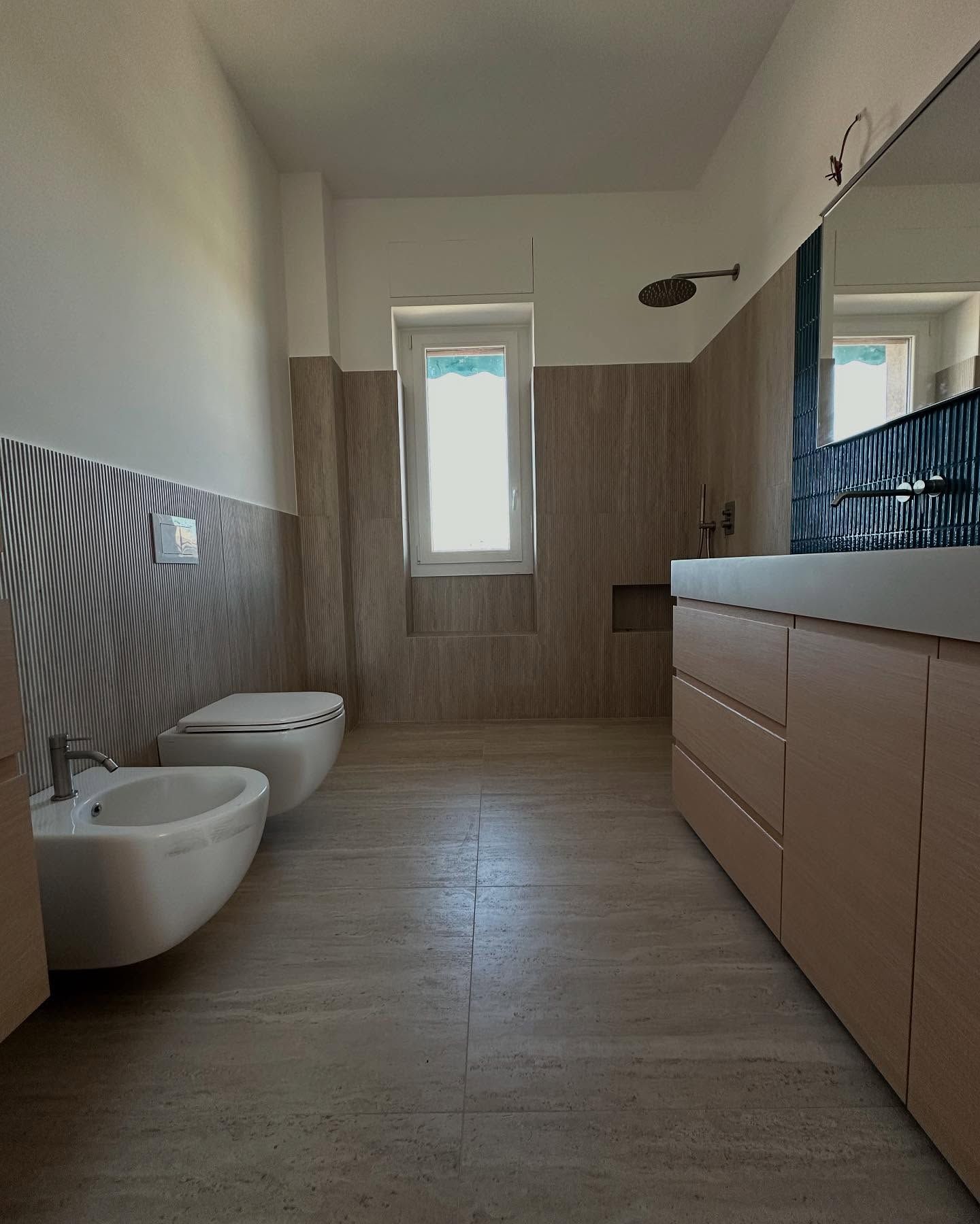 Bagno moderno con bidet, WC sospeso, mobile lavabo e zona doccia piastrellata in tonalità neutre.