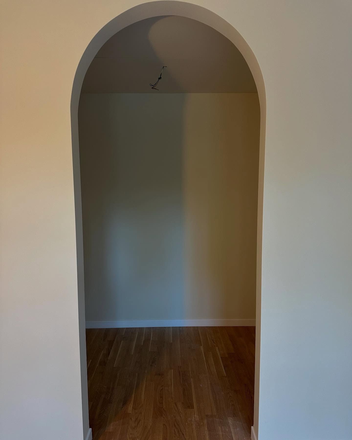Porta ad arco vuota che conduce a una stanza spoglia con pareti bianche e pavimento in legno.