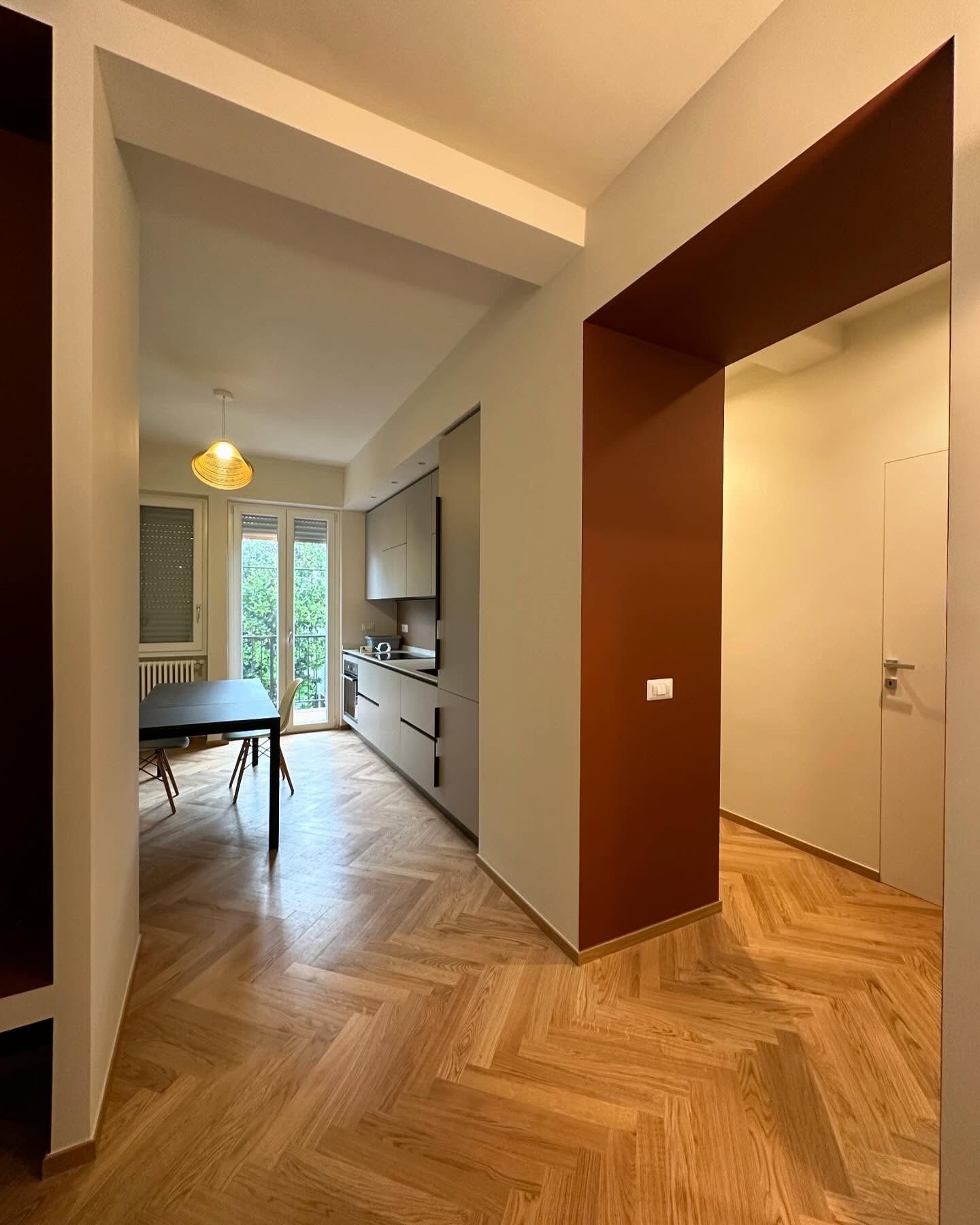Corridoio di un appartamento moderno con pavimento in legno a spina di pesce, cucina a sinistra e porta a destra.