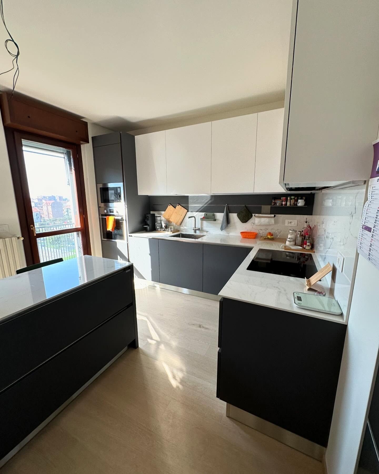 Cucina moderna con mobili in bianco e nero, ripiani bianchi e luce naturale proveniente da una finestra.