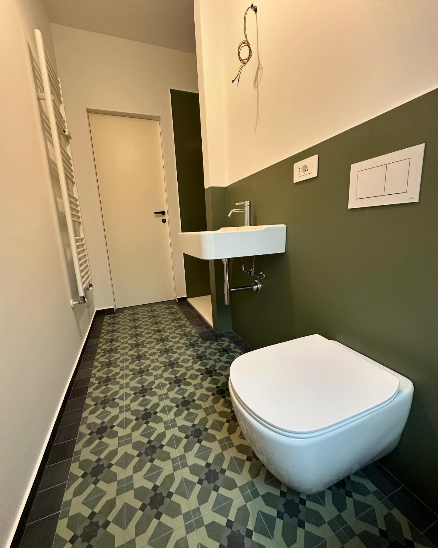 Piccolo bagno con pareti verdi, pavimento decorato, lavabo a parete e WC moderno.