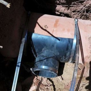 Black plastic drain pipe with metal straps inside a shallow dirt trench