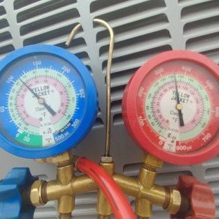 Blue and red HVAC refrigerant gauges with hoses attached to a metal unit