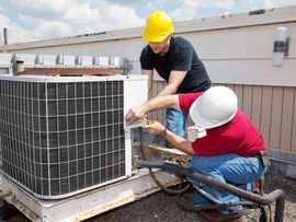 Two workers in hard hats repairing a rooftop air conditioner unit