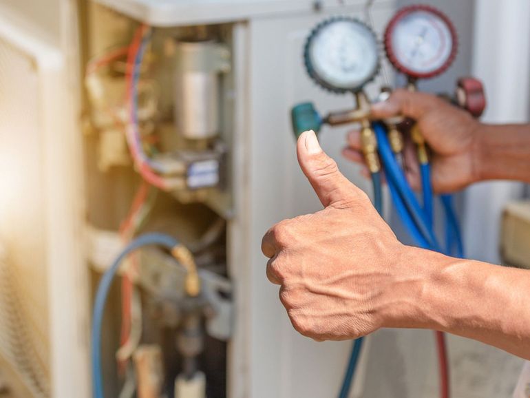 Technician giving thumbs up beside pressure gauges and blue hoses on HVAC equipment