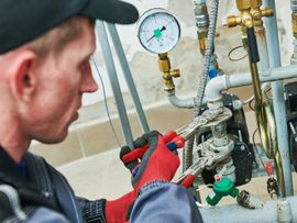 Technician in red gloves repairs plumbing valves and pressure gauge on industrial pipes.