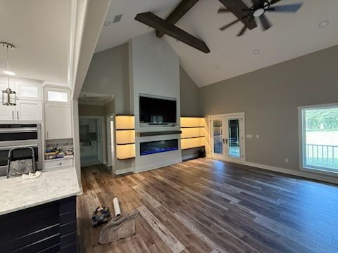 Spacious modern living room with vaulted ceiling, dark wood floors, fireplace, and large windows