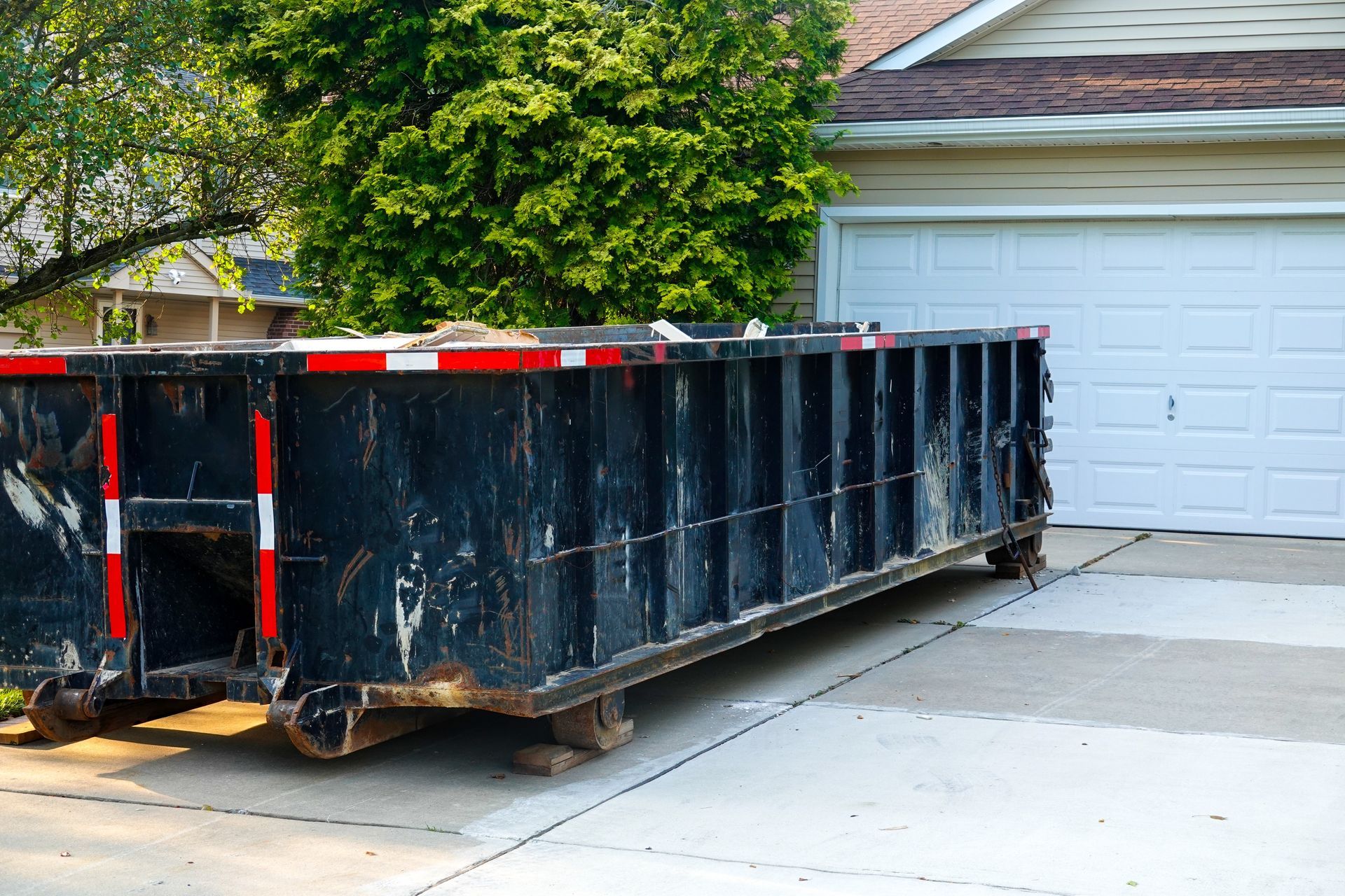 Black dumpster in a driveway next to a closed white garage door.