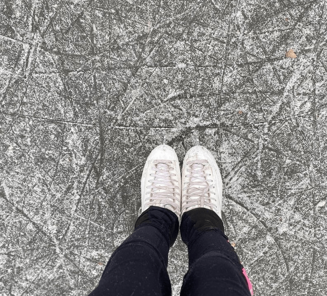 A person is standing on a ice rink wearing white sneakers.