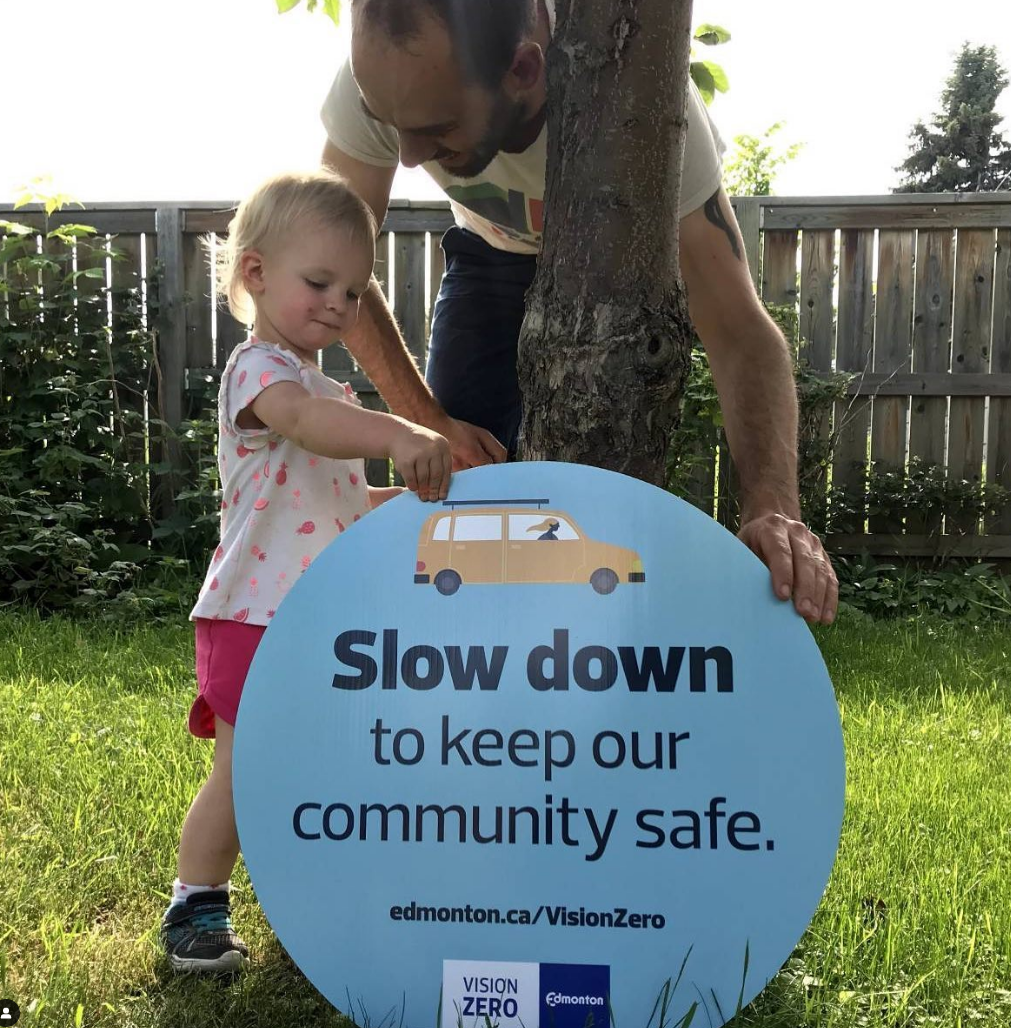 A man and child holding a sign that says slow down to keep our community safe