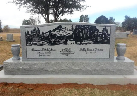 Gray granite headstone with engraved deer and trees in a cemetery field.