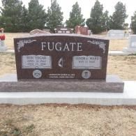 Brown granite FUGATE cemetery headstone with two inset plaques and flower vases in a grassy cemetery