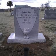 Gravestone in a cemetery with engraved memorial plaque and vase at the base.