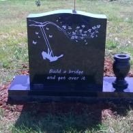 Black memorial gravestone with an engraved swing and quote, set on a bench in a grassy cemetery.
