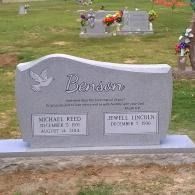 Gray memorial gravestone with engraved names in a cemetery, decorated with flowers in the background