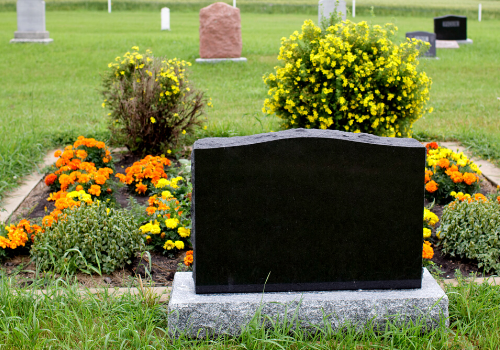 Black gravestone surrounded by orange and yellow flowers in a cemetery