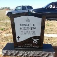Gravestone for Donald K. Minshew with a cross, set outdoors in a cemetery with cars in the background