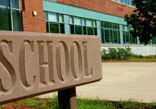 School sign in front of a brick school building with large windows