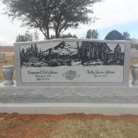 Engraved memorial bench with black mountain and pine scene, set on a stone base outdoors