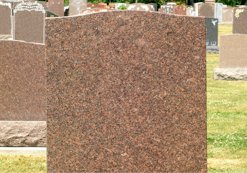 Close-up of a reddish-brown granite gravestone in a cemetery
