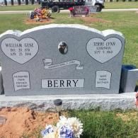 Gray Berry family gravestone in a cemetery, with flowers and a small memorial arrangement behind it.
