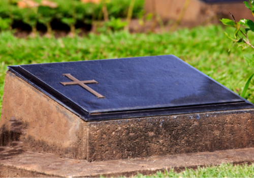 Small gravestone with a dark plaque and cross in a grassy cemetery setting