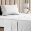 A bed with white sheets and pillows and a lamp.