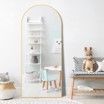 A full length mirror with a white frame is sitting in a room next to a bench.