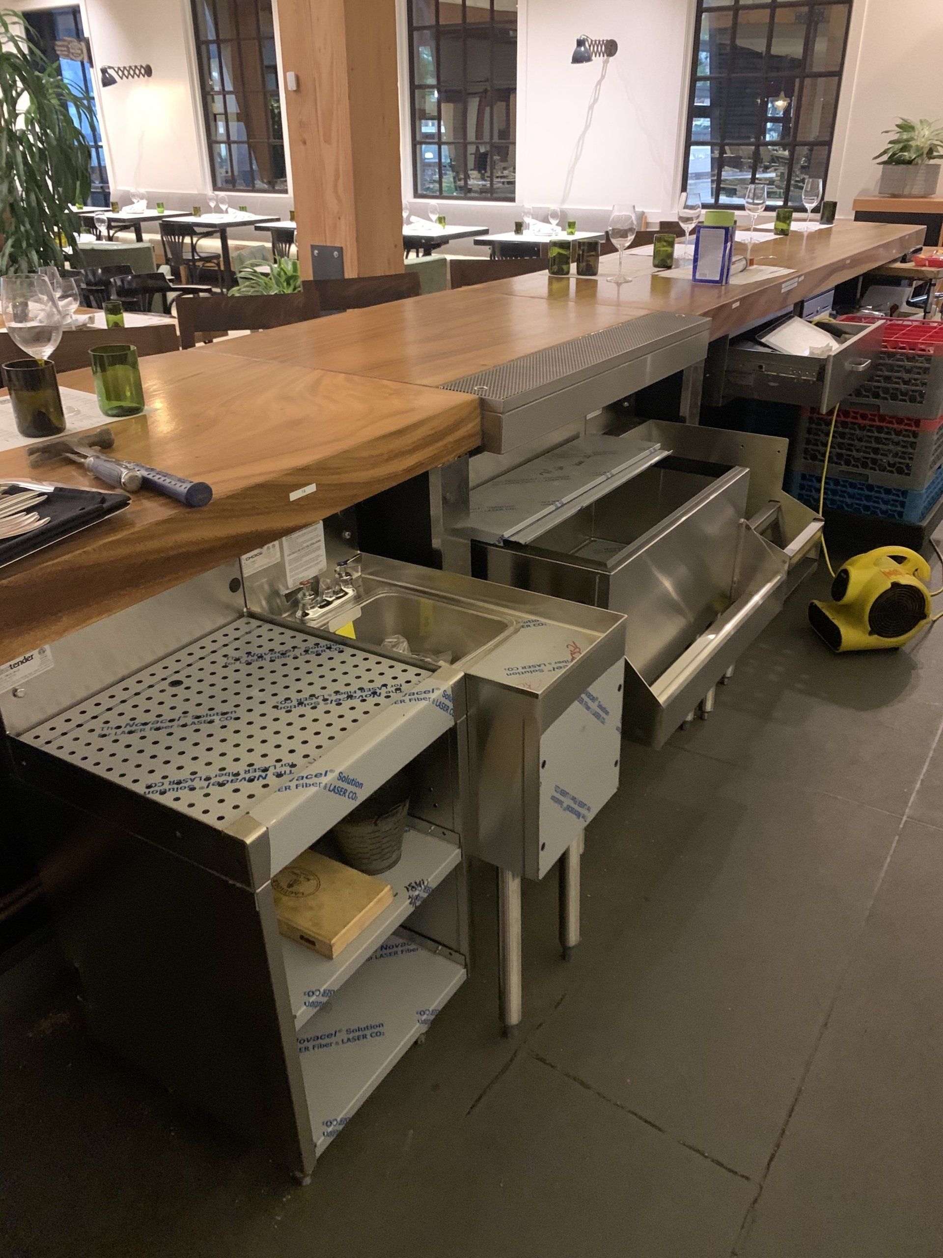 A stainless steel sink is sitting under a wooden counter in a restaurant.