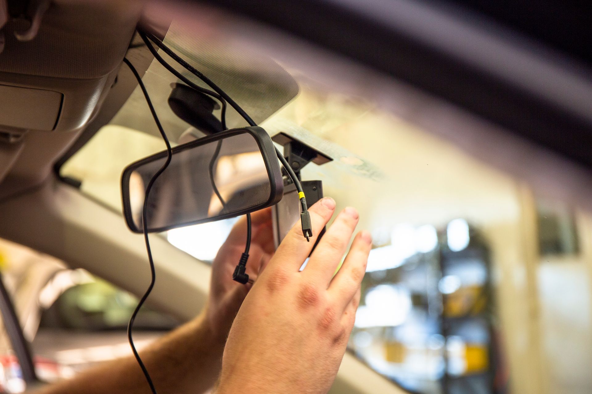 Hand adjusting a rearview mirror in a car with a dangling cable