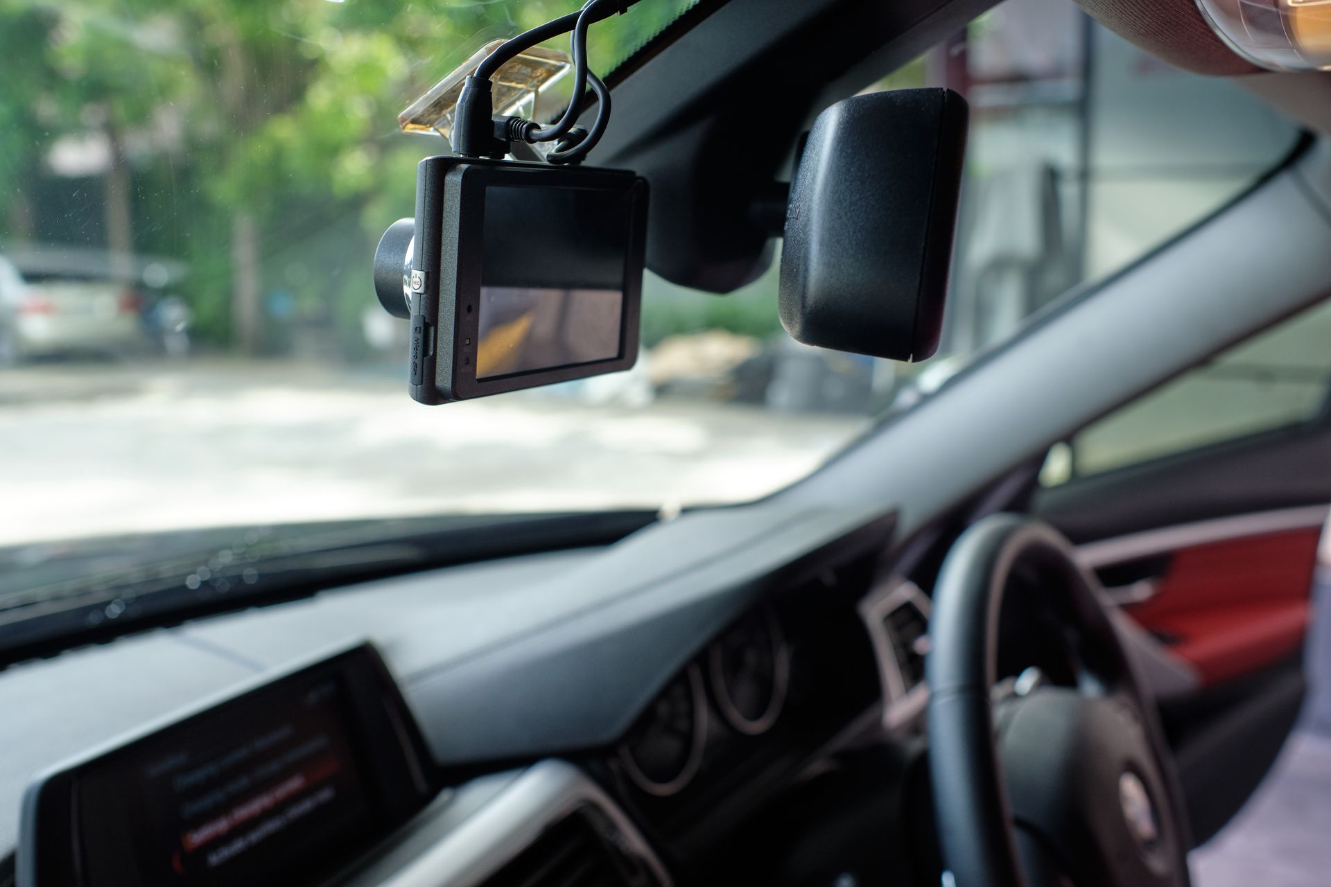 Car interior with dashboard camera mounted near the windshield and a red door panel visible.