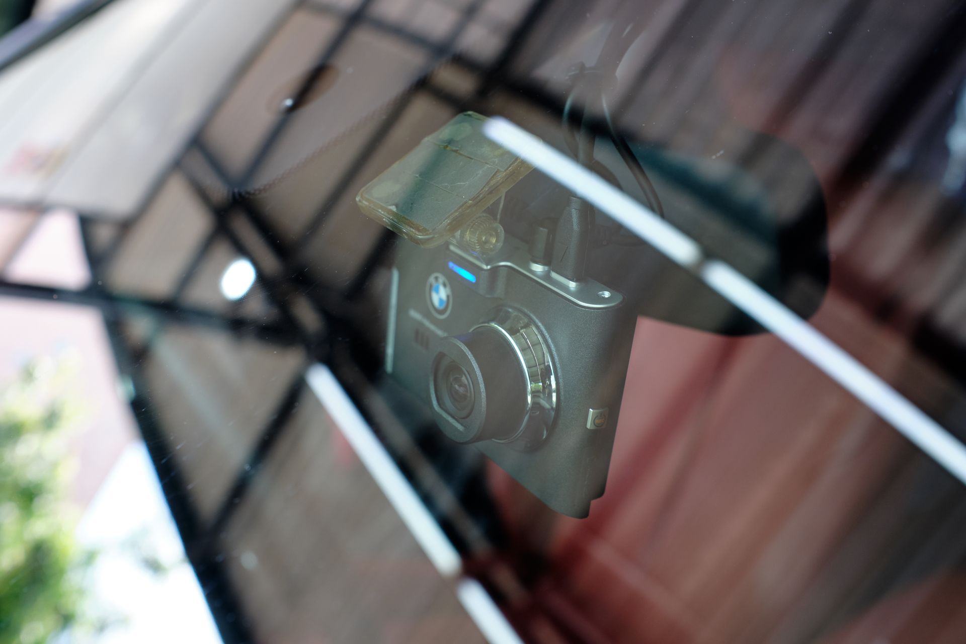Compact camera reflected in a car windshield, with blurred street reflections.