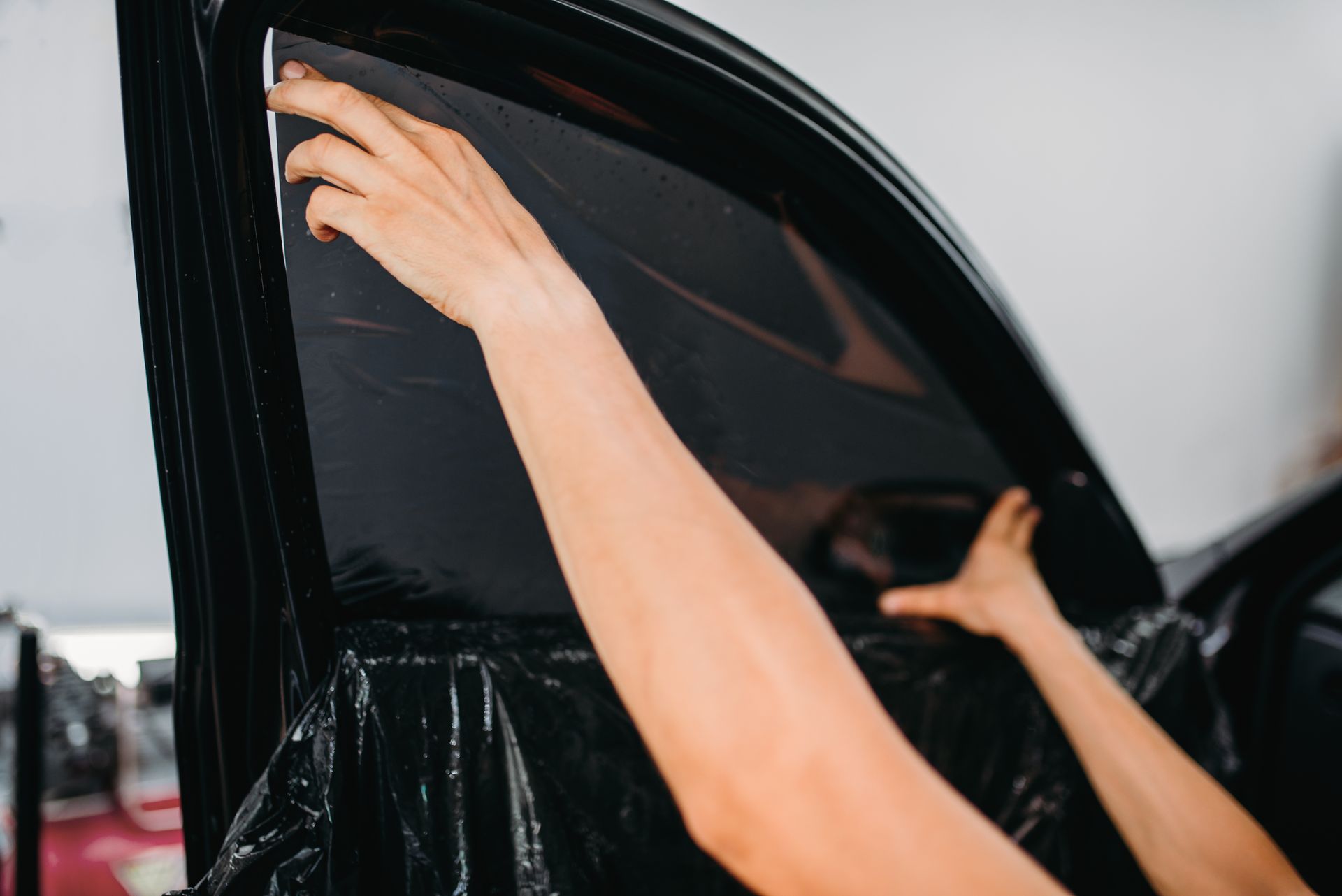 Hands smoothing dark window tint on a car windshield