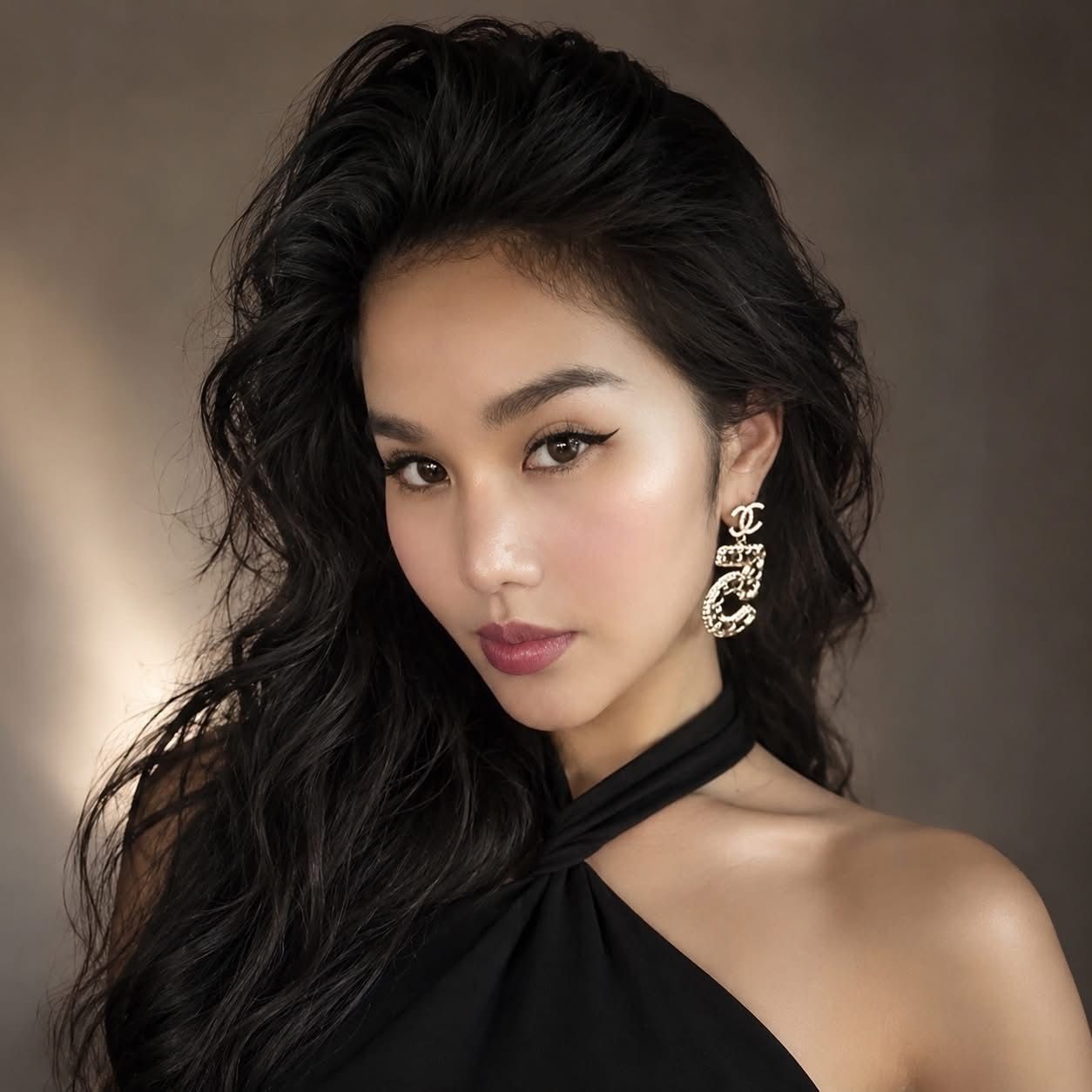 Portrait of a woman with wavy dark hair in a black halter top, wearing ornate earrings, against a soft brown background