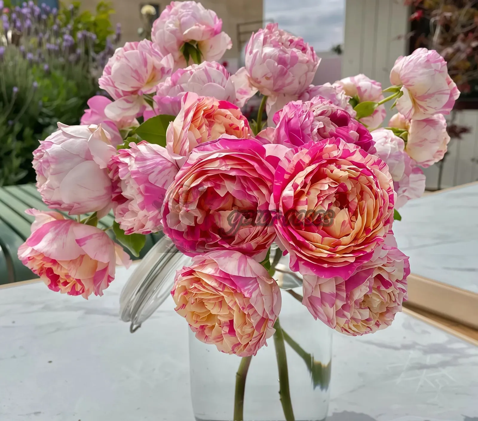 Pink and cream peonies in a glass vase on a table, with a blurred garden background.