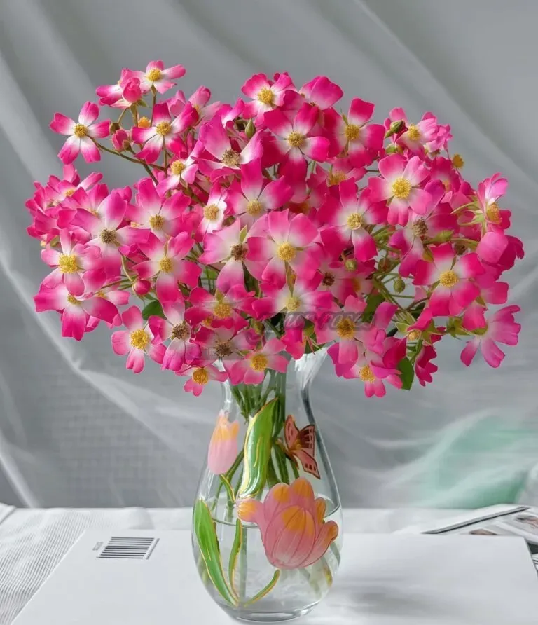 Pink and white flowers arranged in a glass vase on a white tablecloth.