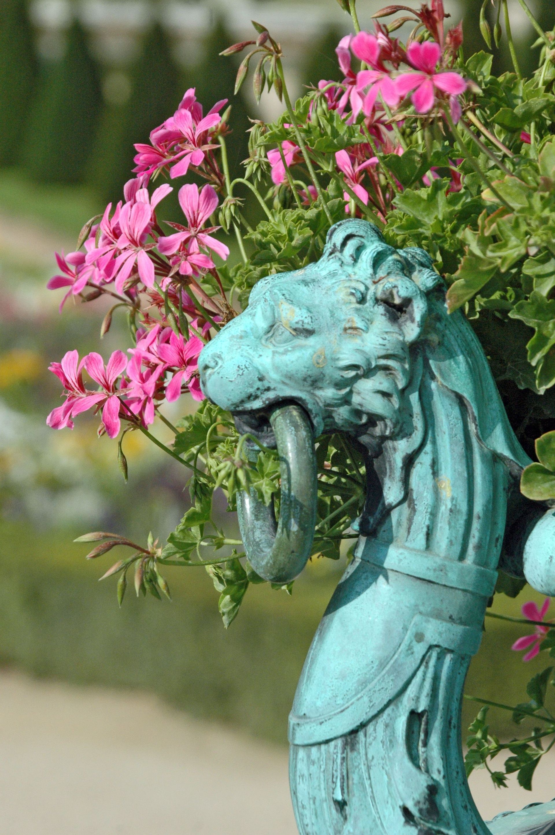 Turquoise dragon statue beside pink flowers in a garden